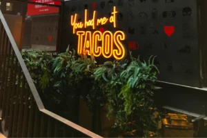 Illuminated tacos lettering among restaurant plants