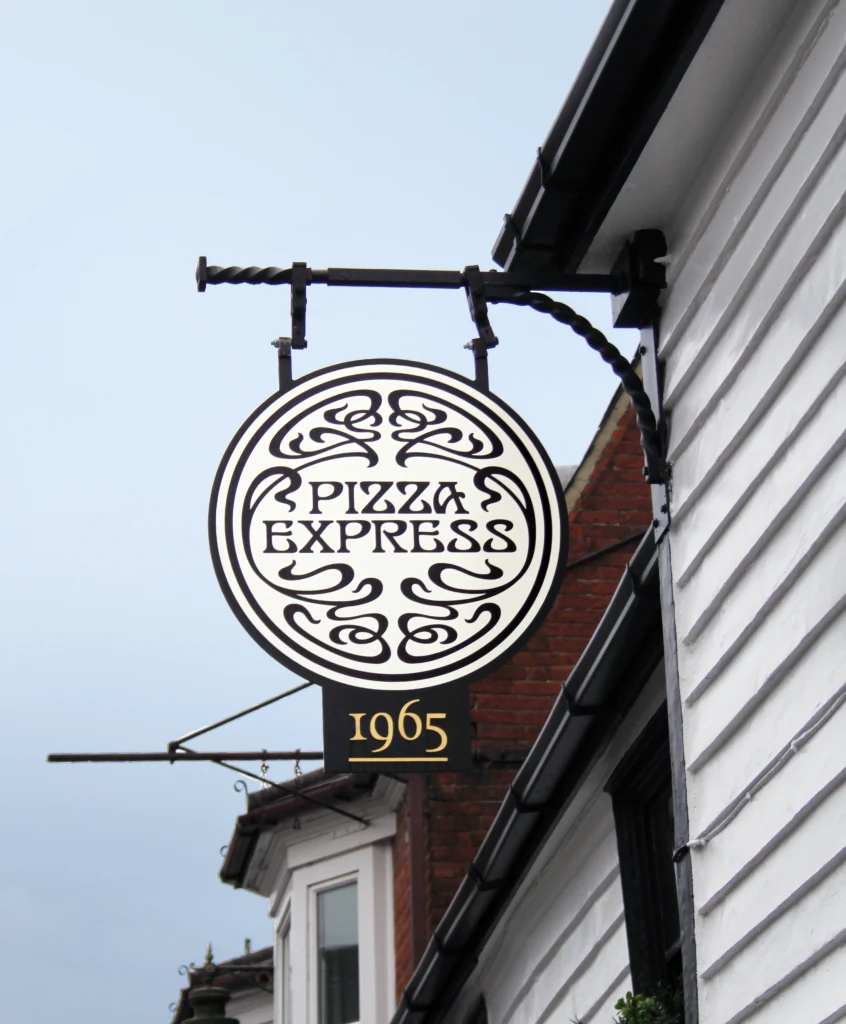 Round PizzaExpress projecting sign mounted on an ornate black metal bracket outside a building